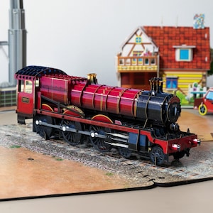 Locomotora roja emergente con motor de vapor y luz LED cubierta con una tarjeta de felicitación de madera - Tren de Hogwarts