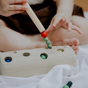 Child using a magnetic rod to catch green worms from a wooden block toy for 3 year old toddler.