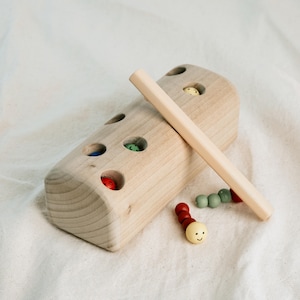 Wooden Montessori toy with magnet rod catching a red and blue worm, shown on neutral fabric.