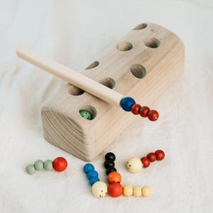 Montessori wooden worm game showing magnetic rod and toy block on soft surface.
