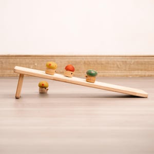 Puede incluir: Cuatro setas de juguete de madera con tapas de diferentes colores ruedan por una rampe de madera. Las setas son amarillas, rojas, verdes y amarillas con puntos rojos. La rampe está hecha de madera clara y tiene una ligera inclinación.