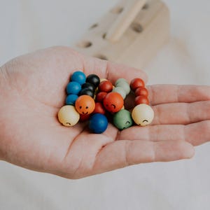 Hand holding multiple colorful wooden worm toys with happy faces, ideal for toddlers.