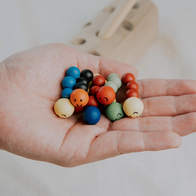 Hand holding multiple colorful wooden worm toys with happy faces, ideal for toddlers.