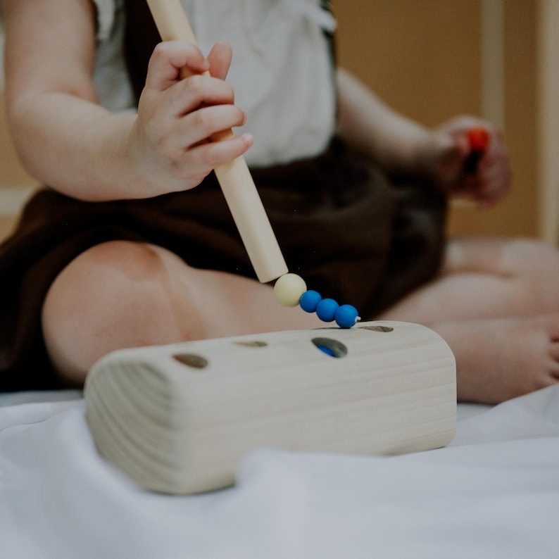 Toddler playing with wooden magnetic worm toy, improving fine motor and hand-eye coordination.