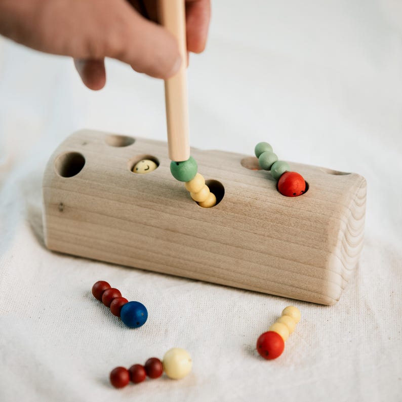 Toddler catching a red worm with a magnetic stick from Montessori wooden block toy.