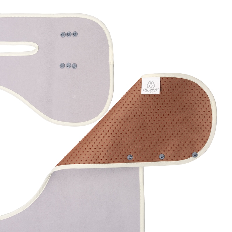 K&ouml;nnte beinhalten: Ein hellgraues und braunes Babyprodukt mit wei&szlig;em Rand und Druckkn&ouml;pfen. Die braune Seite hat ein strukturiertes, gepunktetes Muster. Das Produkt tr&auml;gt den Text "SPLASHPAD" auf einem wei&szlig;en Etikett.