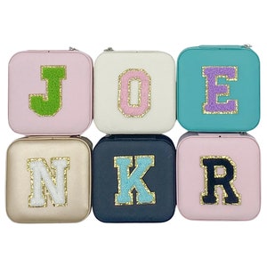 May include: Six small square boxes with different colored lids and a single letter on each lid. The letters spell out the name "JOKER". The letters are made of white fluffy material with gold trim.