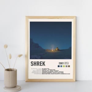 Puede incluir: Un póster enmarcado de la película "Shrek". La imagen muestra una escena nocturna con una fogata. El póster incluye el título de la película, el año y los créditos. El marco es de color madera clara.
