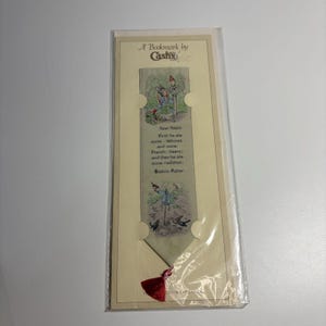 Puede incluir: Un marcapáginas de tela tejida de Cash's con una ilustración de Peter Rabbit y texto de Beatrix Potter. El marcapáginas es de color beige claro con gráficos coloridos de conejos, una borla roja en la parte inferior y presentado en una tarjeta crema.