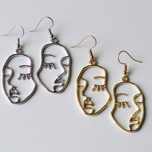 May include: Two pairs of earrings with a face design. One pair is silver and the other is gold.
