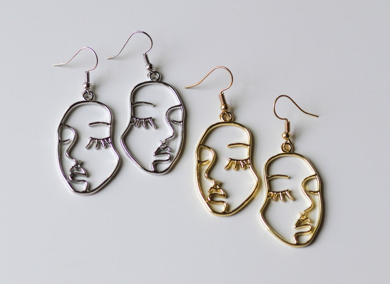 May include: Two pairs of earrings with a face design. One pair is silver and the other is gold.