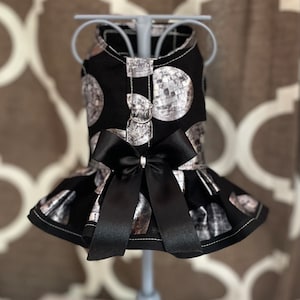 May include: A black dog dress with a silver disco ball print and a black satin bow. The dress has a ruffled skirt.