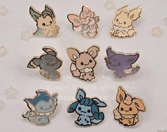 May include: Nine enamel pins featuring various cartoon creatures in pastel colors. Each pin has a gold-colored outline and depicts a different character with unique features. The pins are arranged on a white surface with star-shaped embellishments.