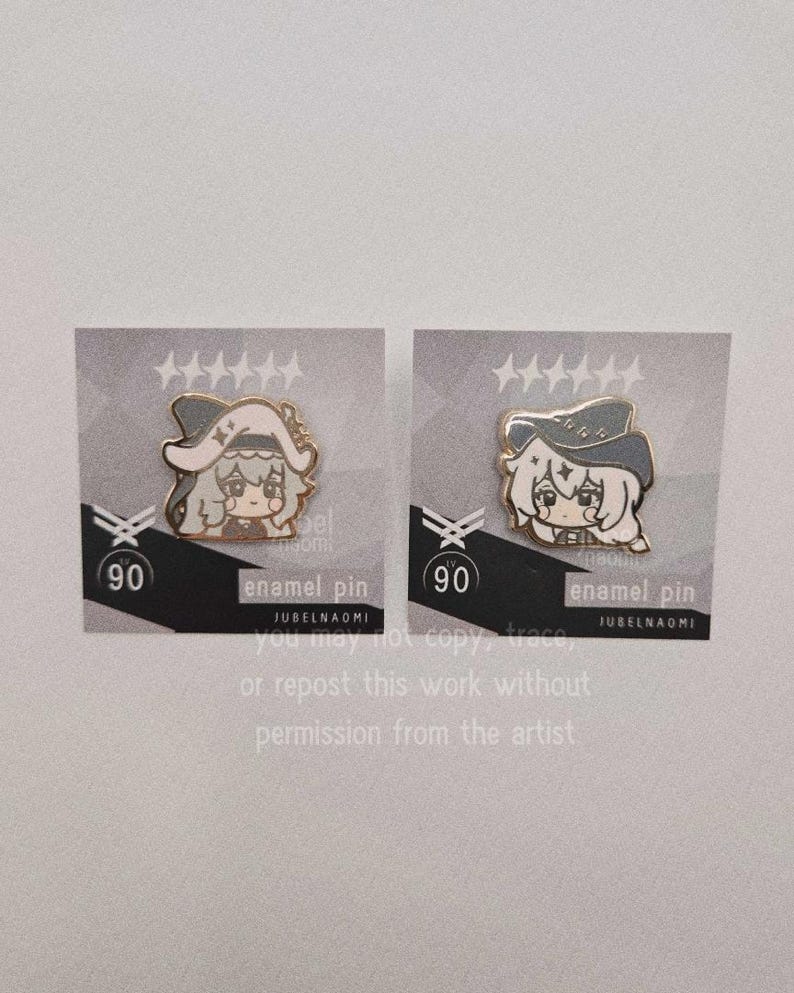 May include: Two enamel pins featuring a cartoon character with a hat. The pins are on gray cards with the number 90 and the text "enamel pin" and "JUBELNAOMI". The pins have a gold outline and are in a cartoon style.