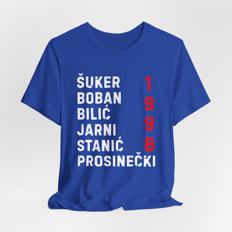 May include: Royal blue t-shirt with white text listing names and the red number 1998. The names are &Scaron;UKER, BOBAN, BILIĆ, JARNI, STANIĆ, and PROSINEČKI. The shirt is a crew neck.