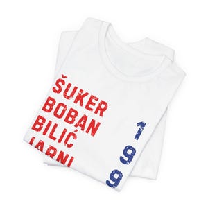 May include: White t-shirts with the names &Scaron;UKER, BOBAN, BILIĆ, and JARNI printed in red, and the number 1999 in blue. The shirts are folded and stacked on top of each other.