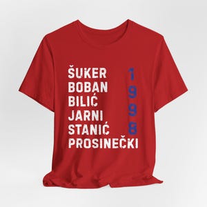 May include: Red t-shirt with white text listing names and the blue number 1998. The names are &Scaron;UKER, BOBAN, BILIĆ, JARNI, STANIĆ, and PROSINEČKI. The shirt is made of a soft material.