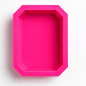 Puede incluir: Un molde de silicona rosa brillante, de forma rectangular con bordes biselados. El molde vacío se encuentra sobre un fondo blanco. La forma recuerda a una gema o una pequeña bandeja, adecuado para manualidades o repostería.