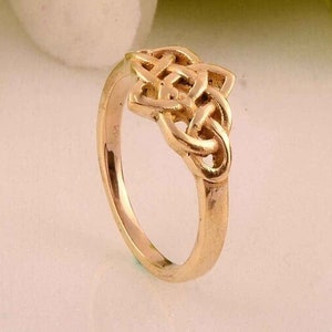 May include: A gold-colored ring with a Celtic knot design. The ring is simple and elegant.