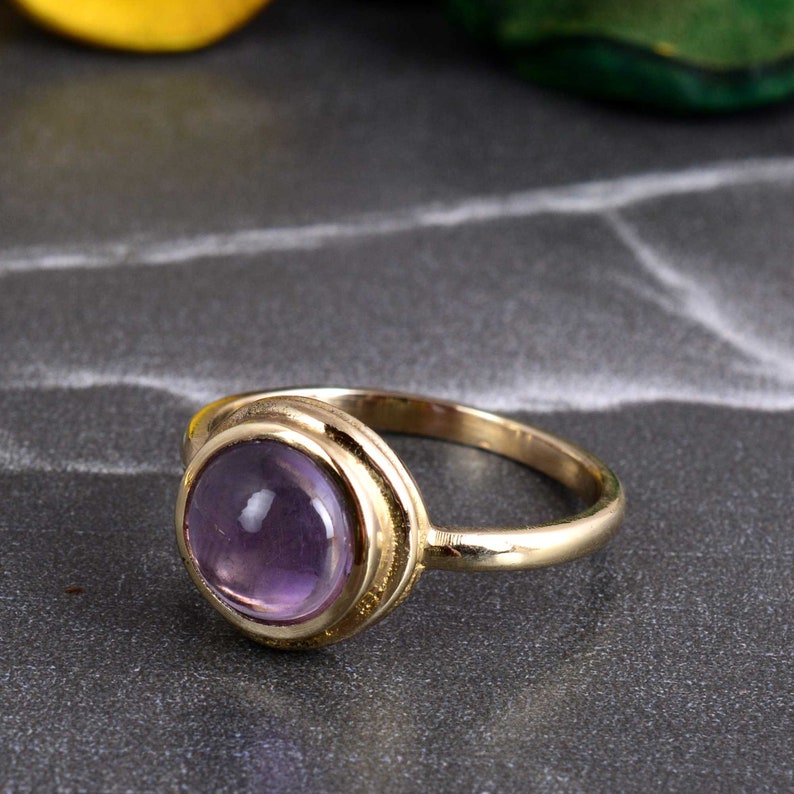 May include: A gold ring with a purple amethyst gemstone set in a bezel setting.