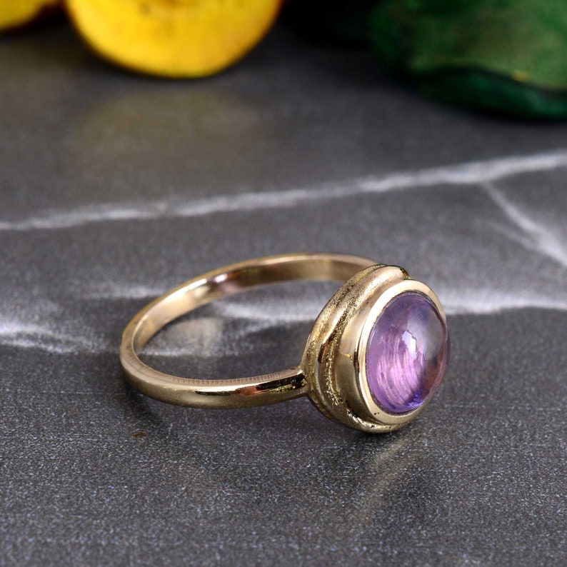 May include: A gold ring with a purple gemstone set in a bezel setting. The ring has a simple band and a smooth finish.