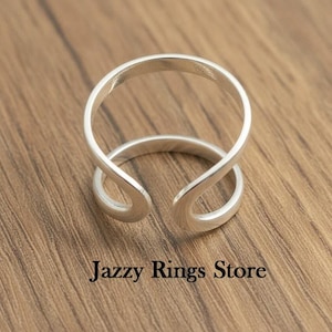 May include: A silver-colored ring with a unique open design. The ring features a double-banded loop that wraps around the finger. The text "Jazzy Rings Store" is displayed at the bottom of the image.
