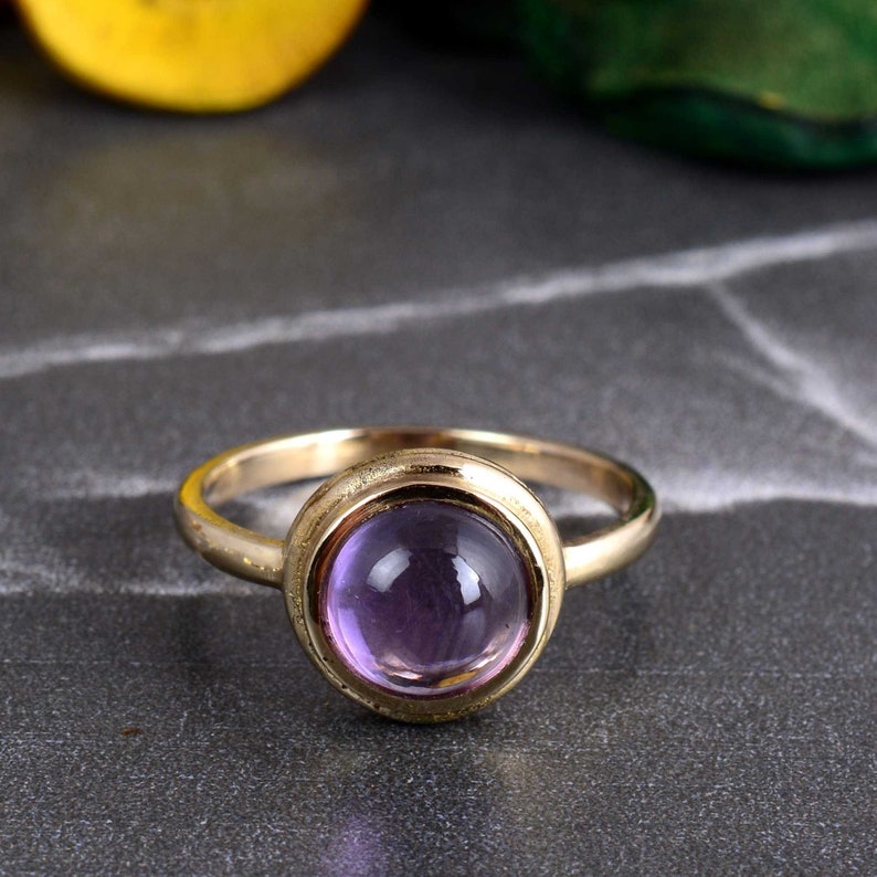 May include: A gold ring with a purple gemstone set in a bezel setting.
