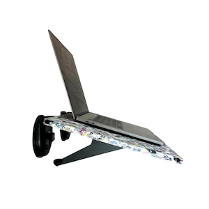 May include: A laptop computer sits on a black and white desk with a colourful, recycled plastic surface. The desk is mounted to a wall with two black brackets.