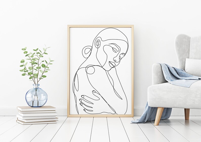 May include: Line art drawing of a person's face and shoulders in a minimalist style. The drawing is in black and white and is framed in a light wood frame.