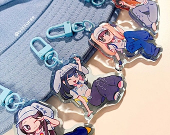 May include: Four acrylic keychains featuring cartoon characters wearing bucket hats and casual clothing, each attached to a light blue lobster clasp. The characters are depicted in various poses and are arranged over a light blue fabric bucket hat.