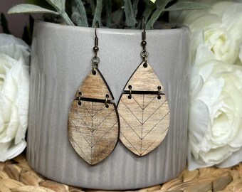 May include: A pair of wooden earrings with a geometric pattern. The earrings are shaped like teardrops and have a light brown color. The earrings are made of wood and have a natural finish.