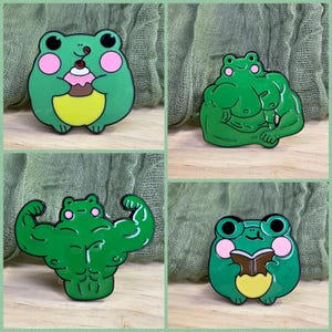 May include: Four green frog enamel pins. One frog holds a cupcake, two are muscular, and one reads a book. Each frog has pink cheeks and black eyes. The pins are on a green background.