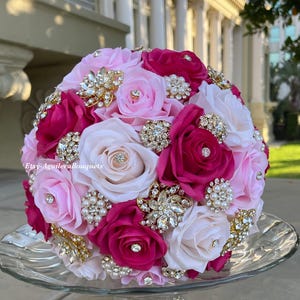 May include: A bridal bouquet made of pink, white, and fuchsia silk roses with gold and rhinestone brooches.