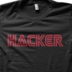 Może przedstawiać: Czarny t-shirt z napisem "HACKER" w czerwonych, blokowych literach na piersi. Tekst ma warstwowy design. Koszulka ma okrągły dekolt i krótkie rękawy. Prosty, swobodny element garderoby.
