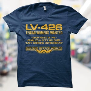 May include: Navy blue t-shirt with the text "LV-426 TERRAFORMERS WANTED" in yellow. The shirt also includes the phrases "GOOD RATES OF PAY," "FAMILIES & PETS WELCOME," and "SAFE WORKING ENVIRONMENT."