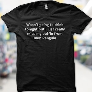 May include: Black t-shirt with white text: "Wasn't going to drink tonight but I just really miss my puffle from Club Penguin." The shirt has a crew neck and short sleeves. The text is centered on the front of the shirt.