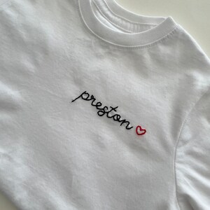 May include: White t-shirt with black embroidered text "preston" and a red heart.