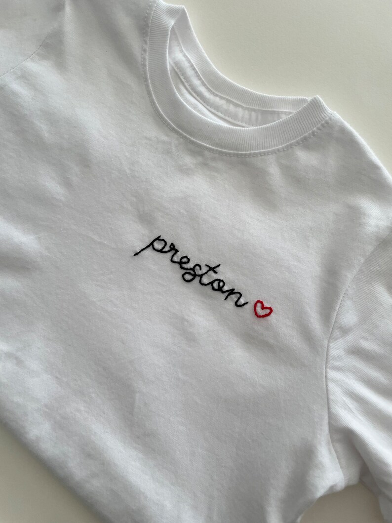 May include: White t-shirt with black embroidered text "preston" and a red heart.