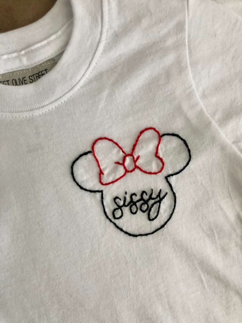 May include: White t-shirt with a black and red embroidered Mickey Mouse head with the word "sissy" written inside.