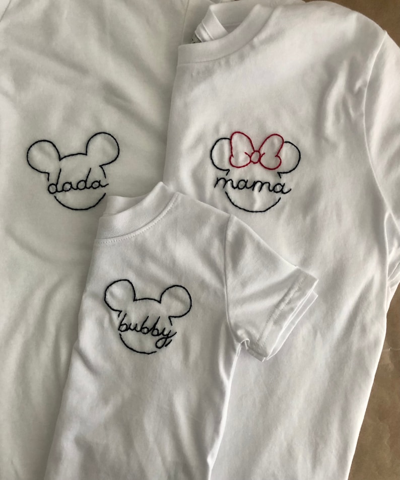 May include: Three white t-shirts with embroidered Mickey Mouse ears and the words "dada", "mama", and "bubby".