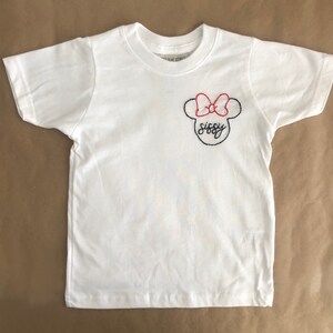 May include: White t-shirt with a black and red embroidered Minnie Mouse design. The design includes a bow and the word "sissy".