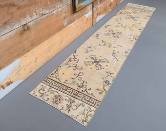 May include: A long, cream-colored rug with a floral pattern and a geometric border. The rug has a subtle distressed look and is perfect for adding a touch of vintage charm to any room.