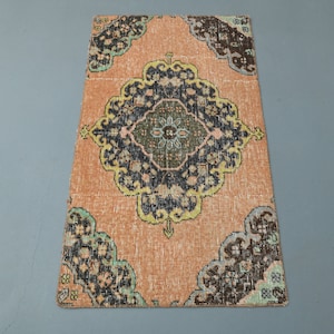 May include: A vintage rug with a central medallion in shades of blue, green, and black on a peach background. The rug has a distressed look and features intricate floral patterns.