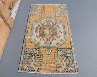 Puede incluir: Una alfombra pequeña y rectangular con un diseño turco tradicional. La alfombra es principalmente amarilla con acentos azules, verdes y marrones. El diseño presenta un medallón central con patrones geométricos.