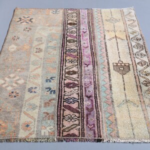 Può includere: Un tappeto vintage con una tavolozza di colori tenui, caratterizzato da una striscia centrale con intricati motivi floreali e geometrici in tonalità di rosa, viola e marrone. Il tappeto ha un aspetto sbiadito e usurato, che aggiunge al suo fascino.