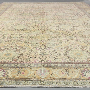 May include: A vintage rug with a cream background and intricate floral patterns in shades of pink, green, and brown. The rug has a border with a repeating design of stylized leaves and flowers.
