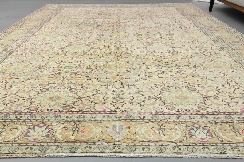 May include: A vintage rug with a cream background and intricate floral patterns in shades of pink, green, and brown. The rug has a border with a repeating design of stylized leaves and flowers.