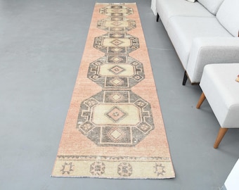 Puede incluir: Una alfombra larga y rectangular con fondo rosa y un patrón geométrico en tonos marrones y crema. La alfombra tiene un borde de flecos.