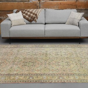 May include: A vintage-style rug with a beige background and intricate floral patterns in shades of brown, pink, and green. The rug has a border with a repeating pattern of small circles and floral motifs.