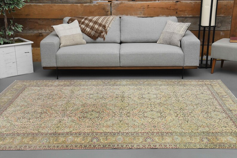 May include: A vintage-style rug with a beige background and intricate floral patterns in shades of brown, pink, and green. The rug has a border with a repeating pattern of small circles and floral motifs.